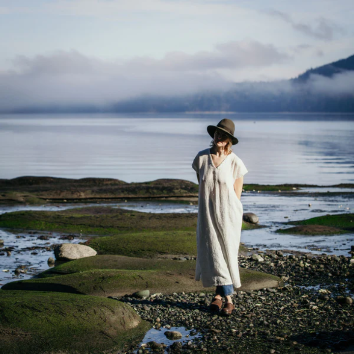 Women's Clothing Canada | Elizabeth Homestead (model in a trendy hat, wearing a comfortable and stylish long linin shirt standing by the water)